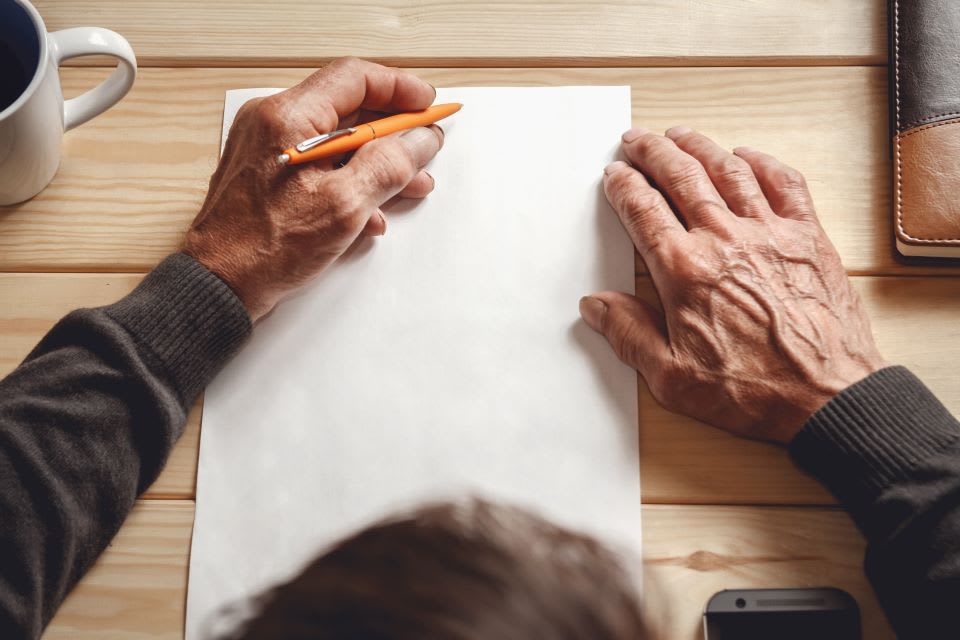 Top view of elderly man's hands as he writes on a blank piece of paper
