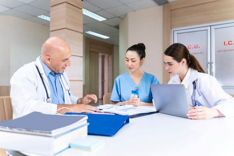 A group of medical professionals sitting at a table looking at nursing care plans.