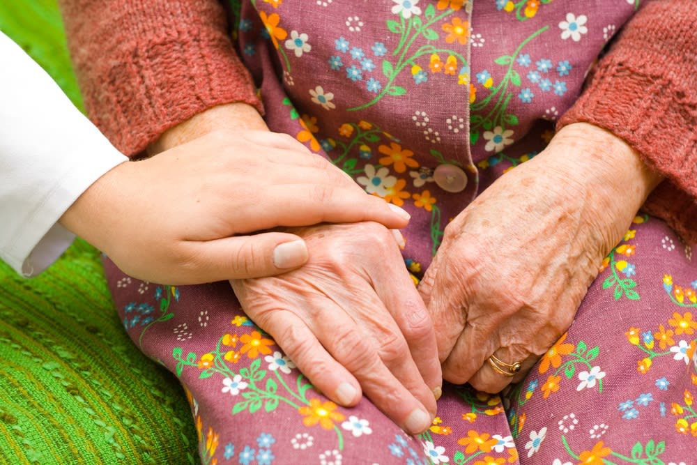 A closeup of a caregiver's hand touching the hand of a senior woman in reassurance