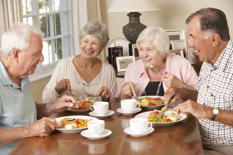Seniors sit around a table enjoying a meal in senior living.