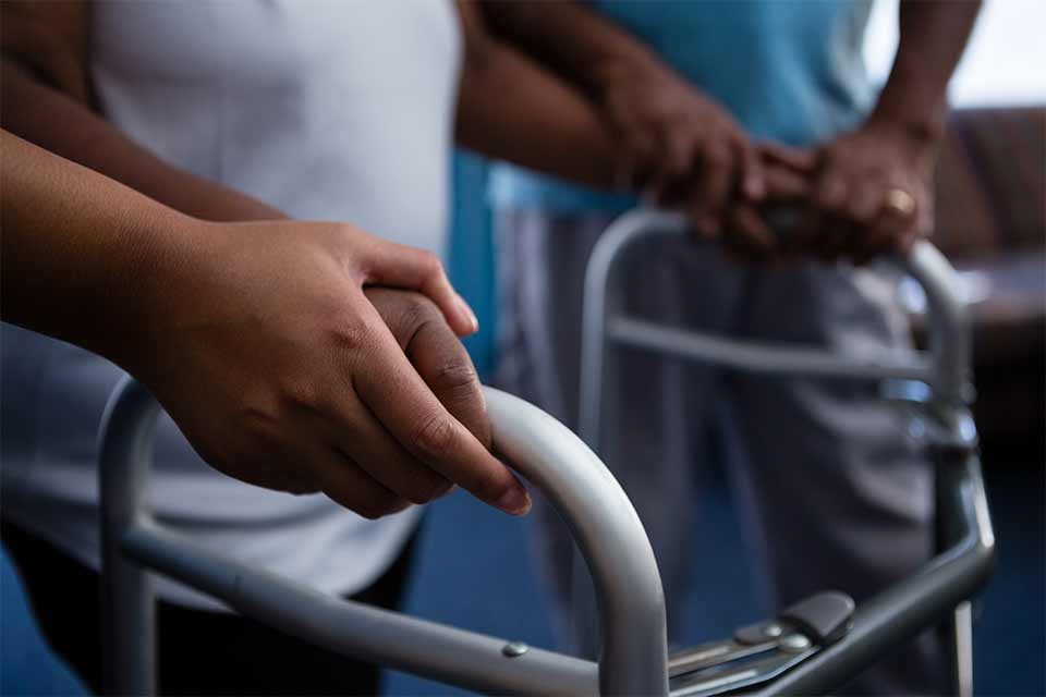 Elderly woman in a nursing home receiving help from a nurse to walk with a walker.